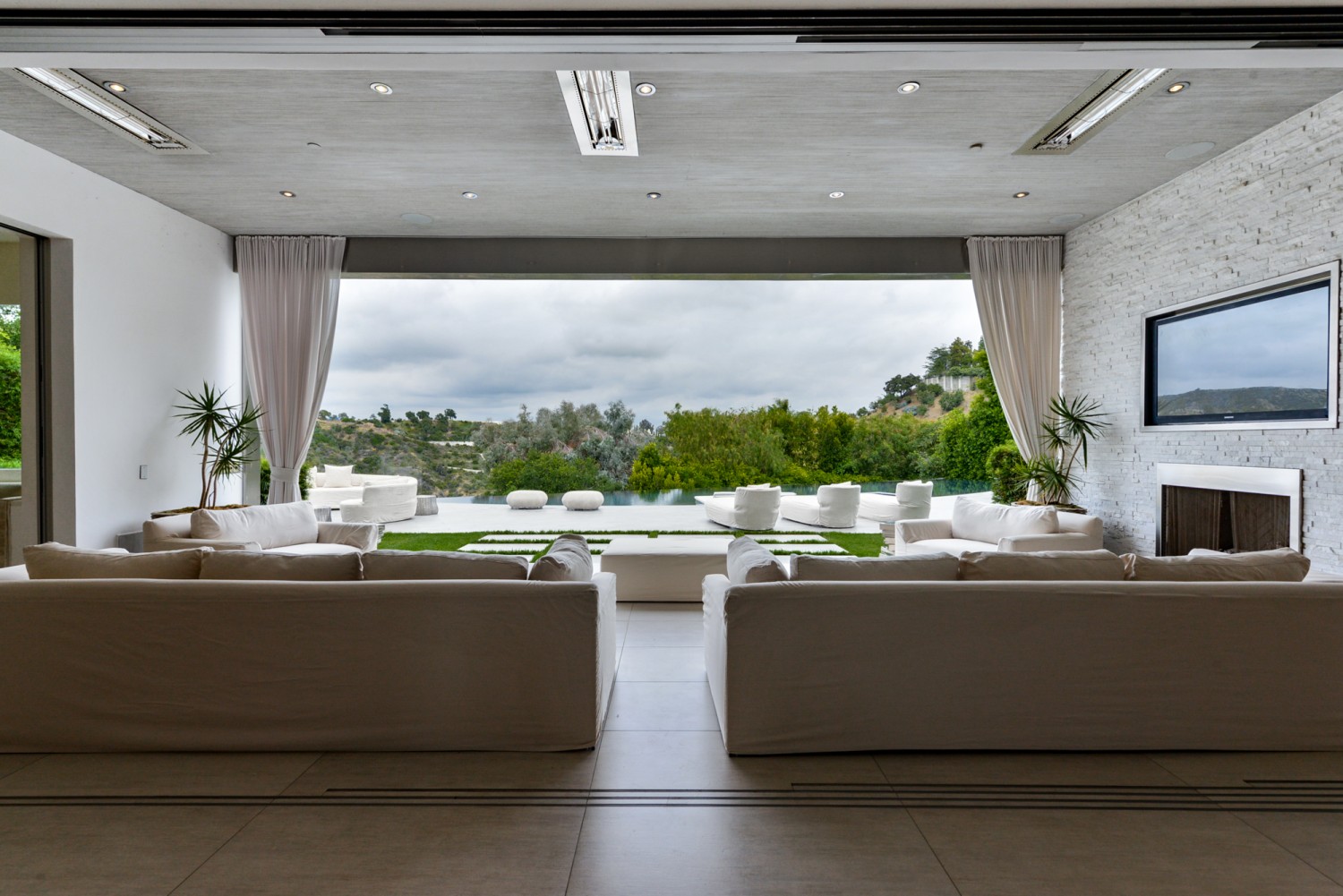 Open great room with retractable walls flowing to the infinity-edge pool and outdoor entertaining terrace overlooking Bel Air.