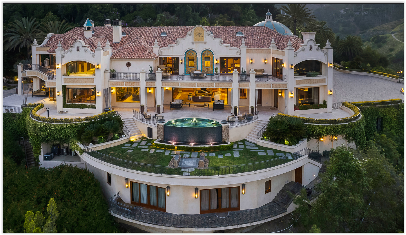 Twilight view of a luxury Mediterranean estate in Los Angeles featuring panoramic city views, elegant architecture, illuminated terraces, and a resort-style water feature.