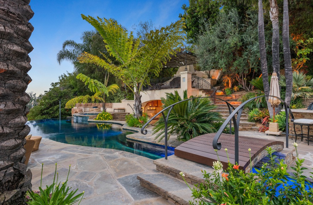 Resort-style swimming pool surrounded by tropical landscaping, stone pathways, and elegant outdoor entertaining spaces.