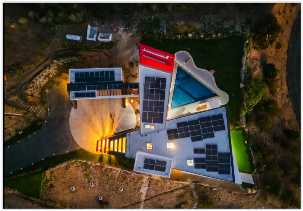 Aerial view of a contemporary Malibu estate showcasing sculptural architecture, rooftop solar panels, a geometric pool, and expansive grounds.