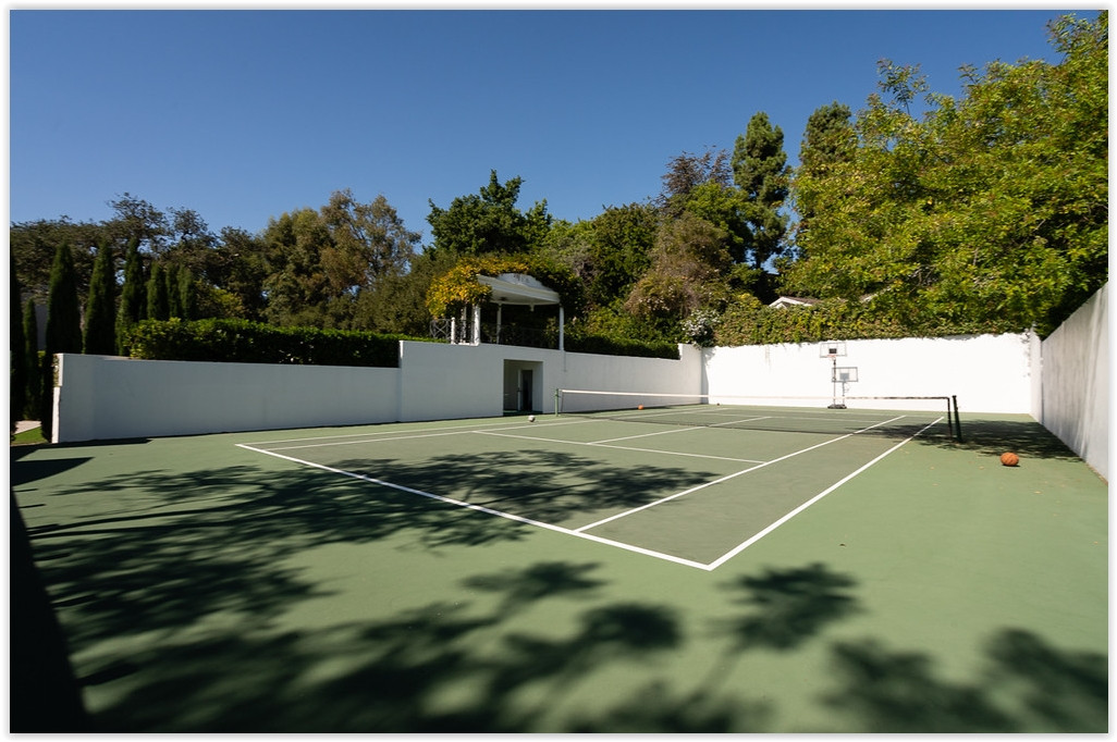 Private tennis court surrounded by mature trees and lush landscaping at a luxury Beverly Hills estate.