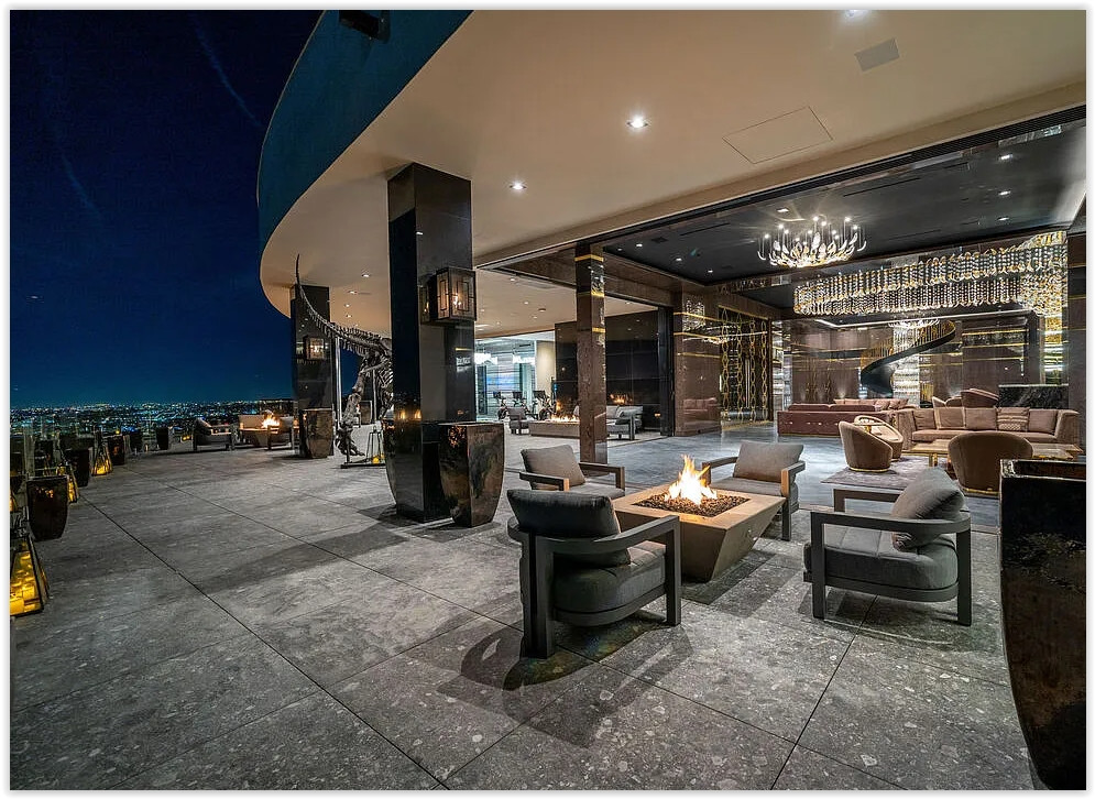 Covered outdoor entertaining terrace with fire feature, elegant lounge seating, and panoramic Los Angeles skyline views at a luxury Bel Air estate.