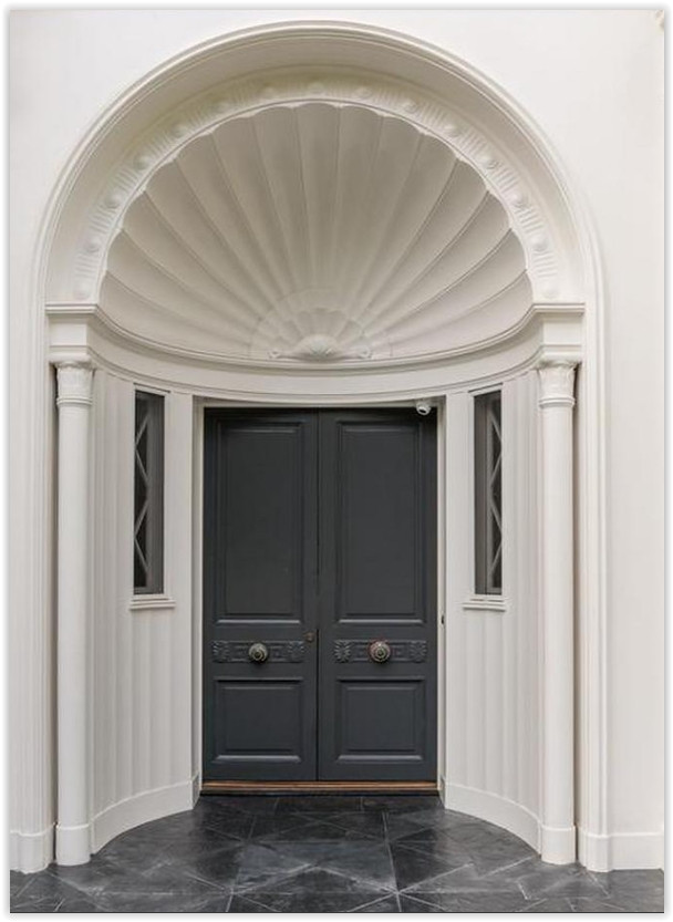 Custom double entry doors beneath an elegant shell-inspired architectural arch at a Beverly Hills estate.