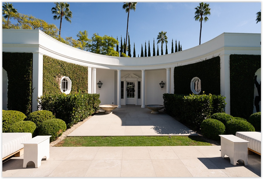 Elegant courtyard entrance with classical columns, sculpted hedges, and timeless architecture at a Beverly Hills estate.