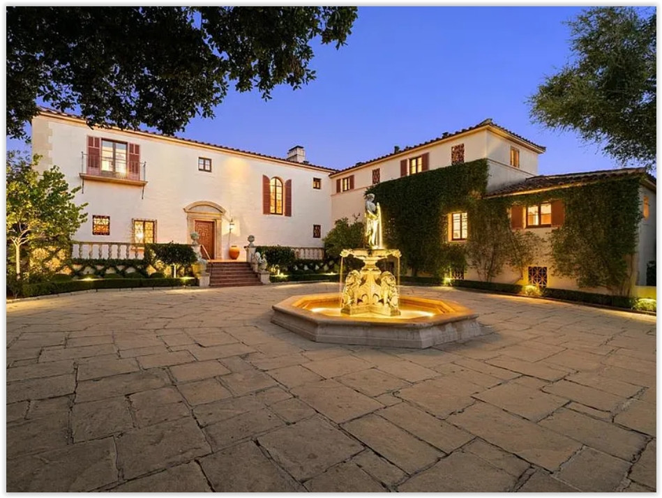 Twilight view of a Spanish Colonial estate with an illuminated courtyard fountain and welcoming entrance.