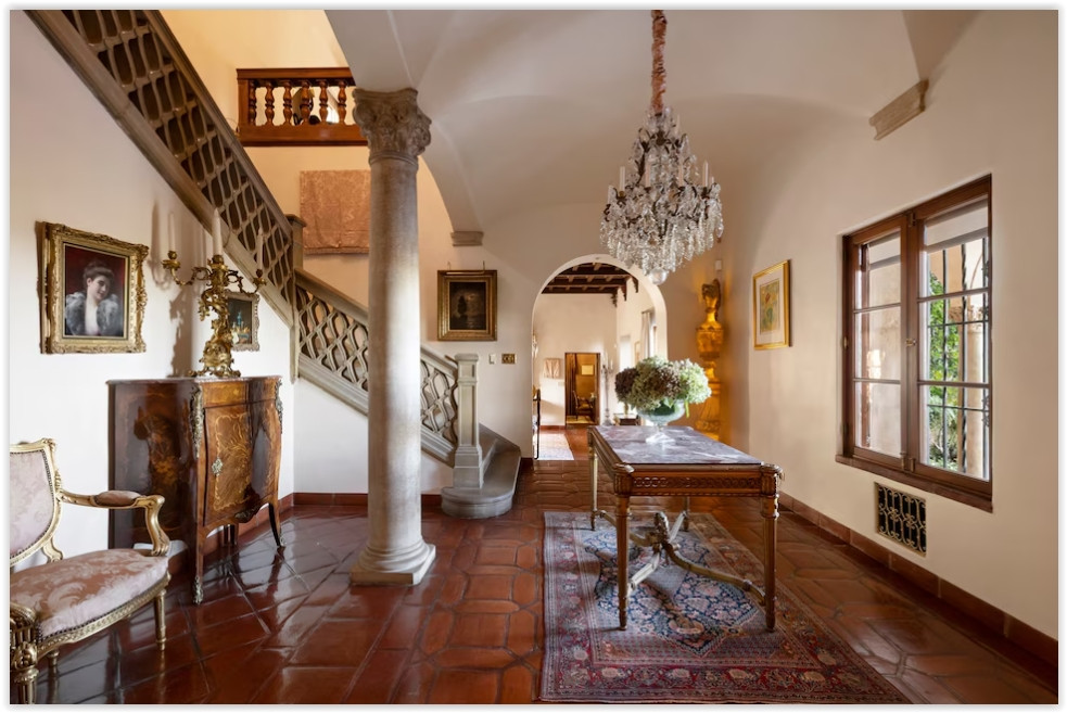 Grand entry hall with terracotta floors, sweeping staircase, crystal chandelier, and handcrafted architectural details.