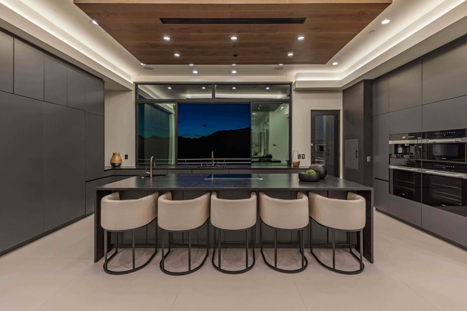 Contemporary open-concept kitchen at Agoura Hills estate featuring large island with seating, modern cabinetry, and expansive window views of surrounding canyon landscape.