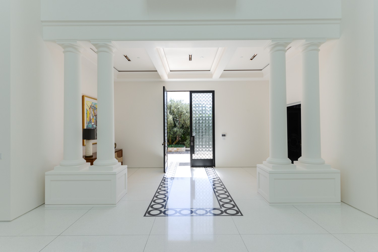 Elegant entry hall with classical columns, patterned flooring and custom front door