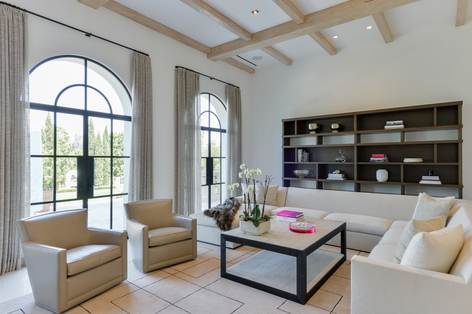 Light-filled living room with arched black-framed doors, exposed beams and neutral furnishings