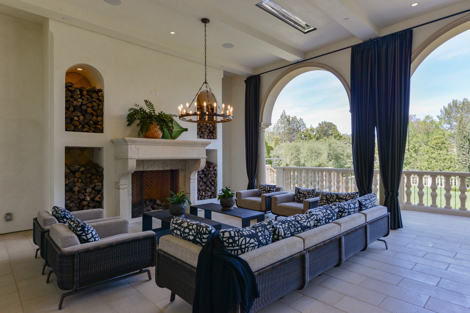 Covered outdoor terrace with fireplace, lounge seating and arched openings overlooking the grounds