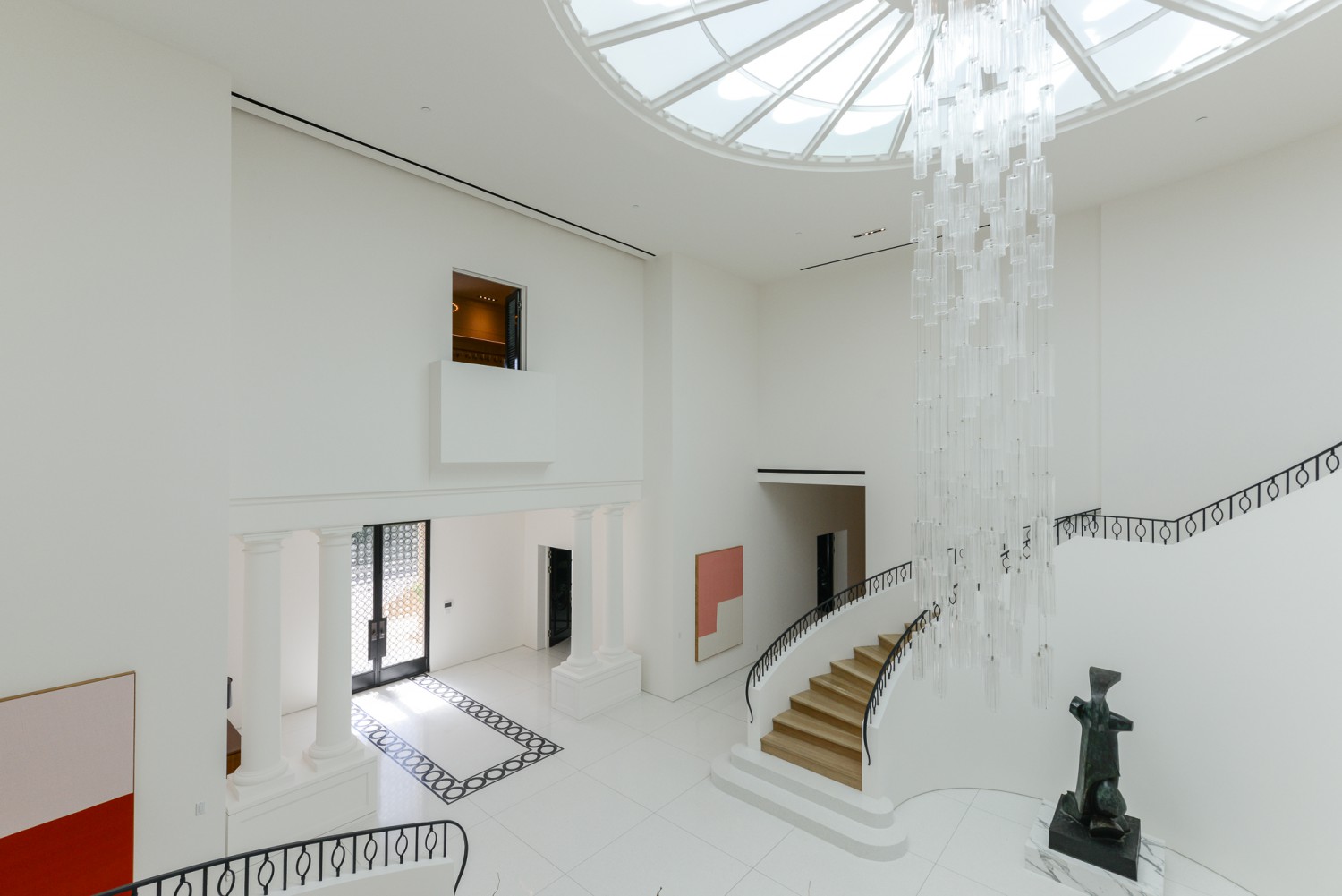 Grand white foyer with double curved staircase, classical columns and skylit chandelier