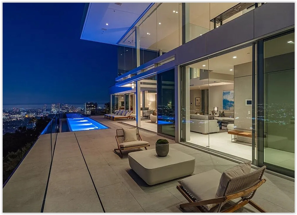 Contemporary glass estate with illuminated infinity pool and expansive outdoor terrace at dusk