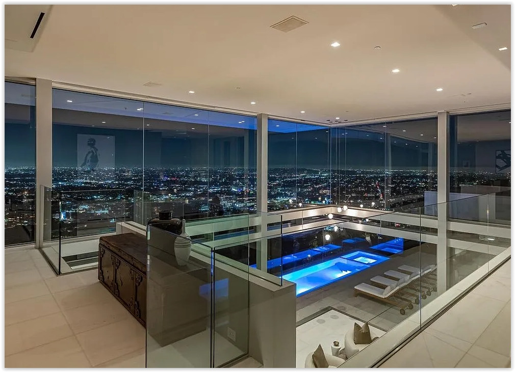 Glass-walled modern interior overlooking an illuminated infinity pool and Los Angeles city lights at night