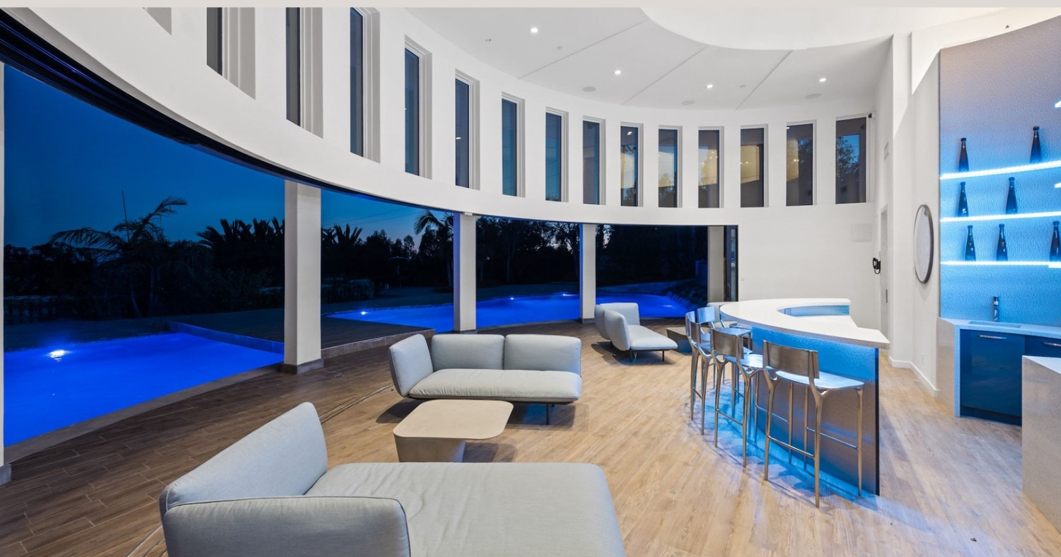 Luxury pool pavilion illuminated at dusk with indoor-outdoor entertaining space overlooking the resort-style pool.