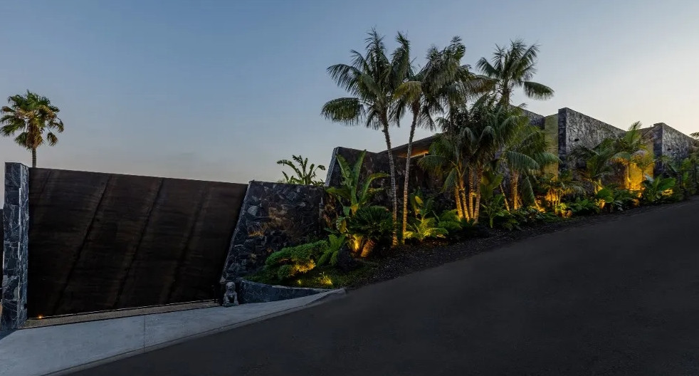 Modern hillside estate exterior with privacy gate and tropical landscaping