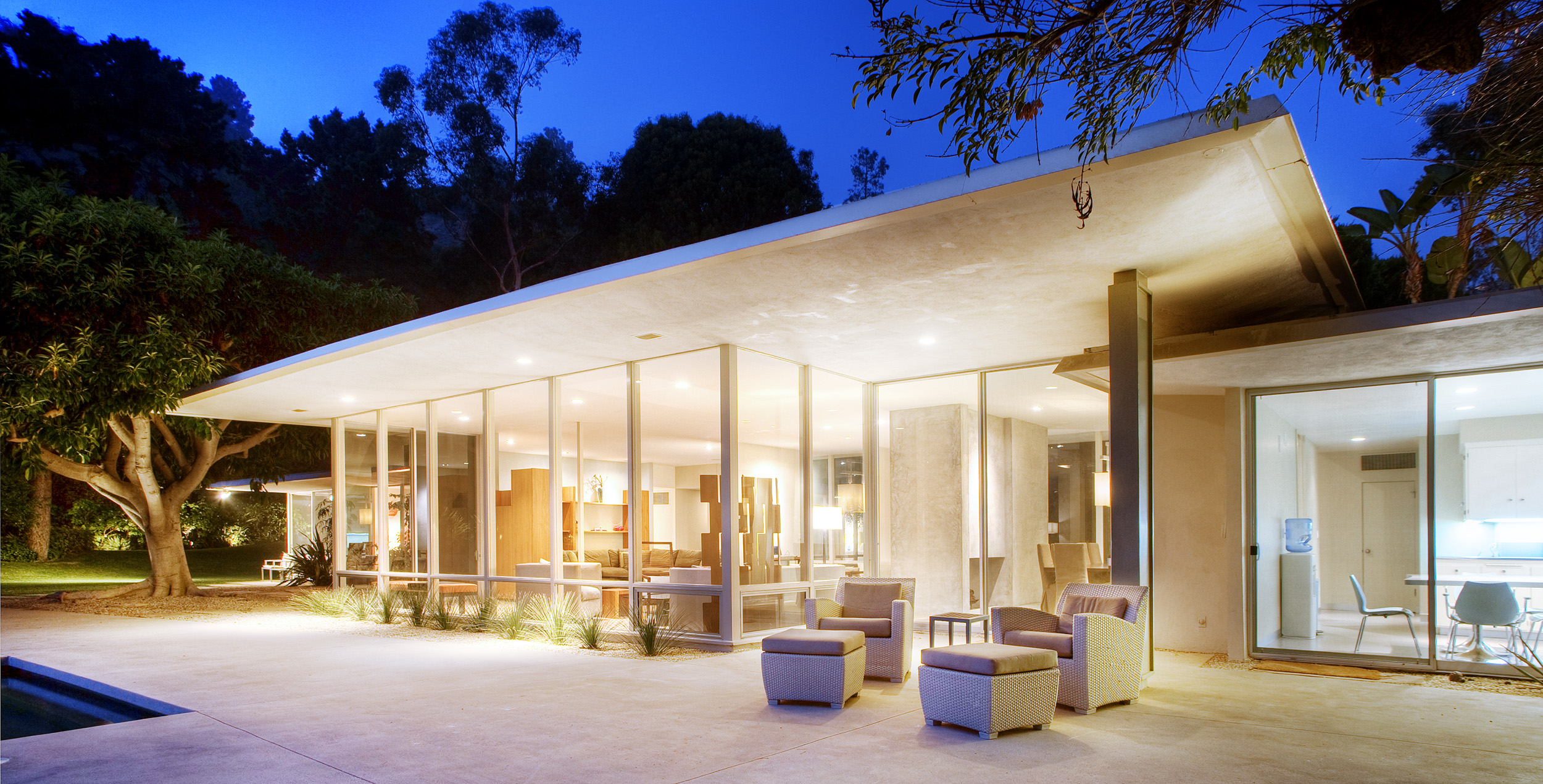 Modern Beverly Hills private event home with glass walls and illuminated outdoor entertaining area at dusk