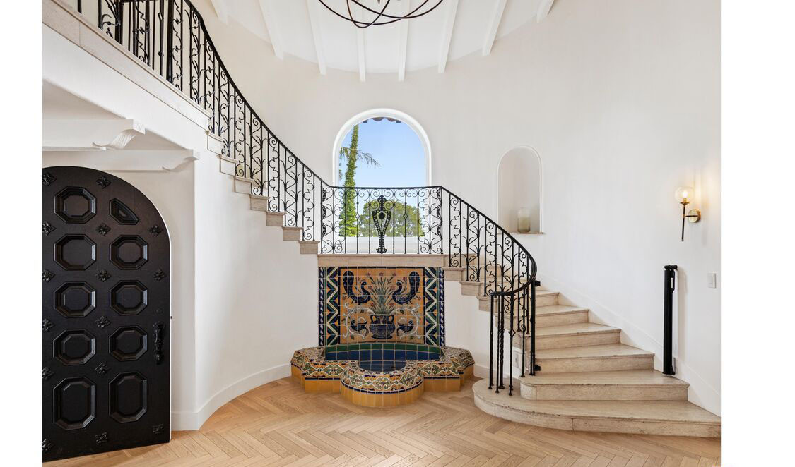 Grand entry hall with curved staircase and decorative tile fountain in Beverly Hills estate