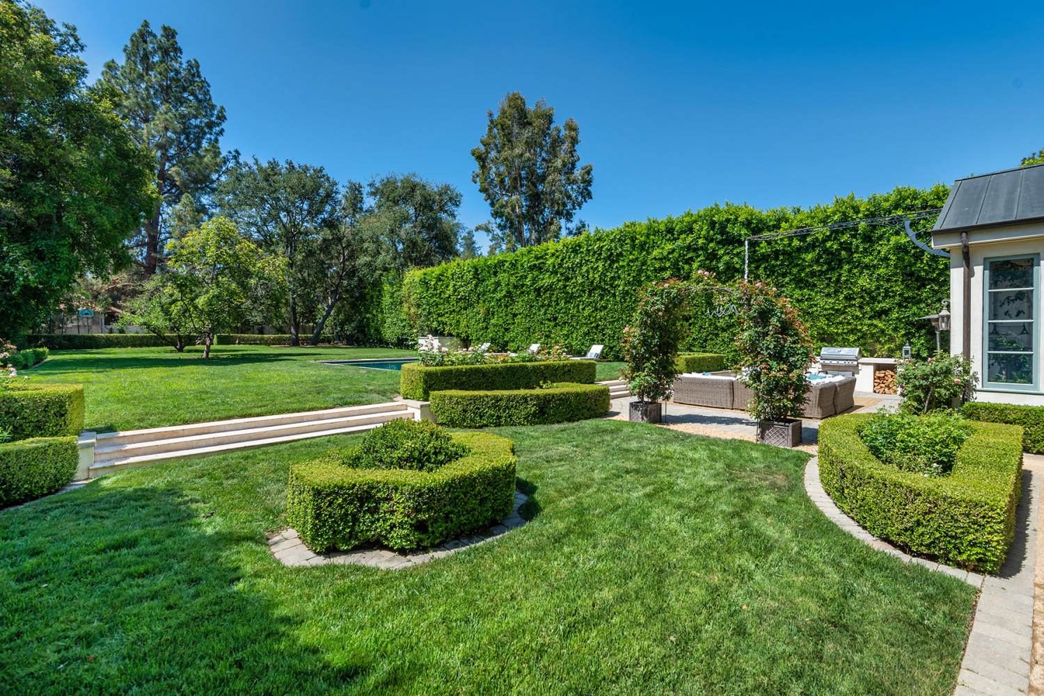Broad lawn with manicured hedges, mature trees and a swimming pool at an Encino garden estate.