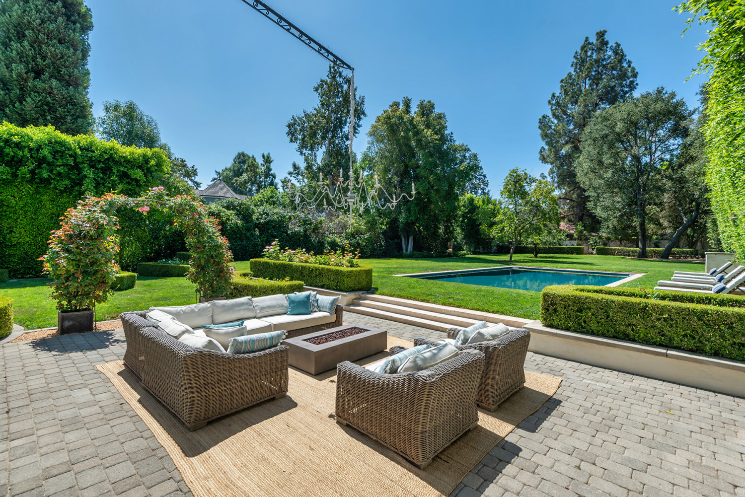Outdoor sofas and a low table on a paved patio overlooking the pool and landscaped gardens at an Encino estate.